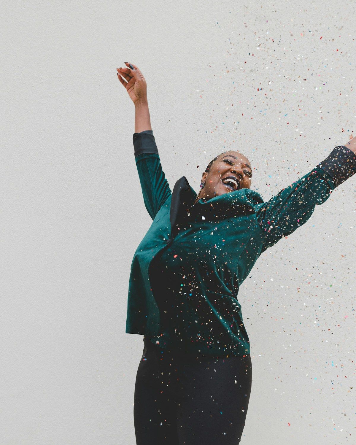A dancer with both arms thrown wide, laughing, as confetti falls.